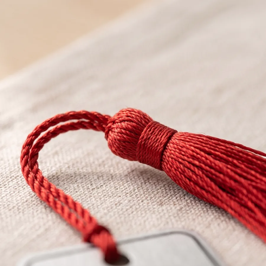 Close do tassel vermelho amarrado à mão no marcador, sobre tecido de linho